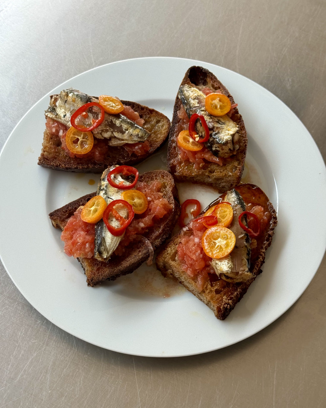Four slices of toasted bread with a topping of sliced chili's, sardines and pureed tomatoes.