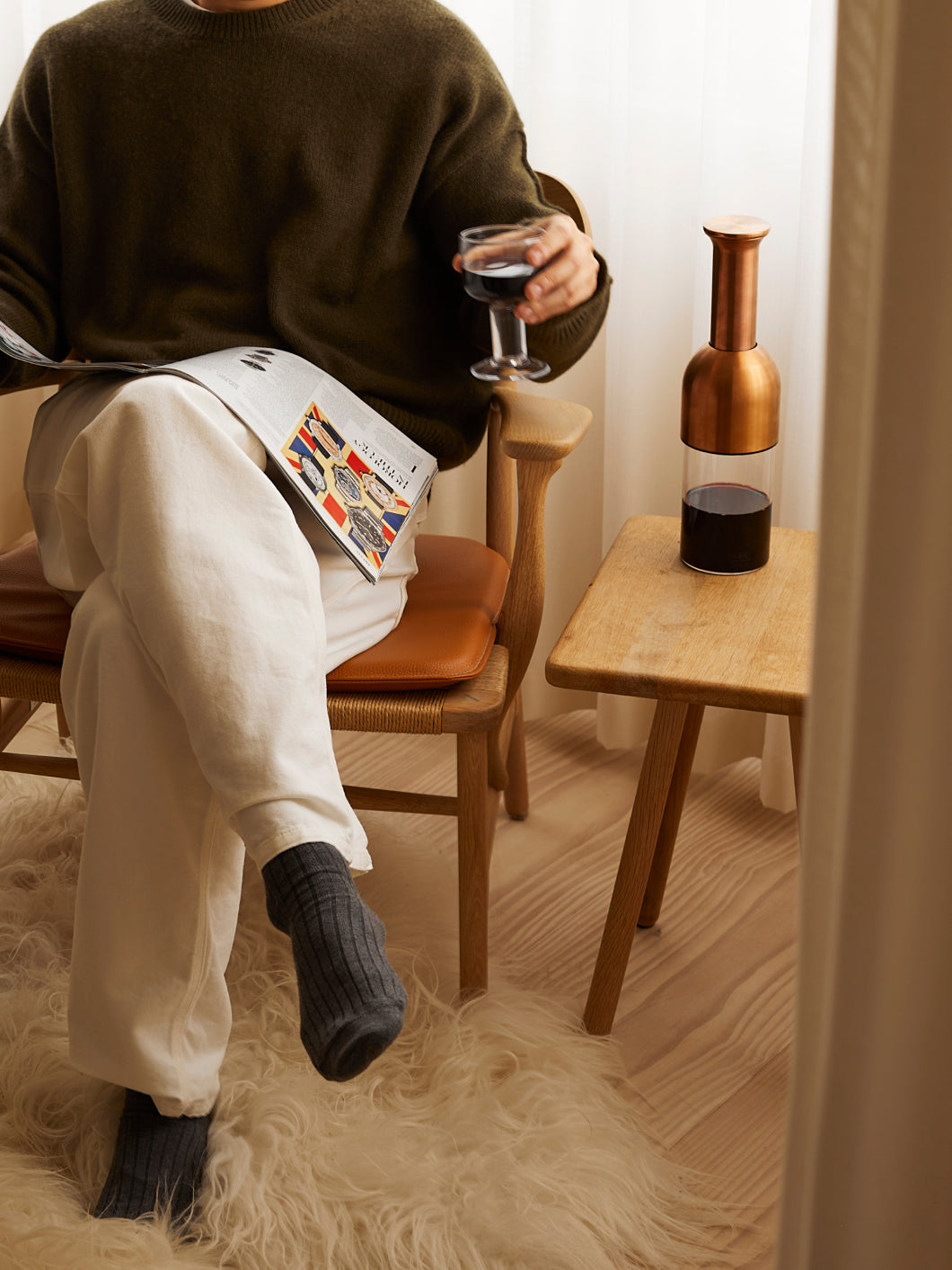 a man sat reading a magazine with a glass of red wine and eto decanter
