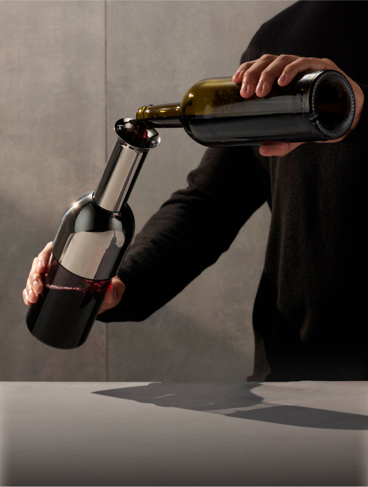 A man pours a bottle of wine into the stainless steel ETO wine decanter on a grey concrete background