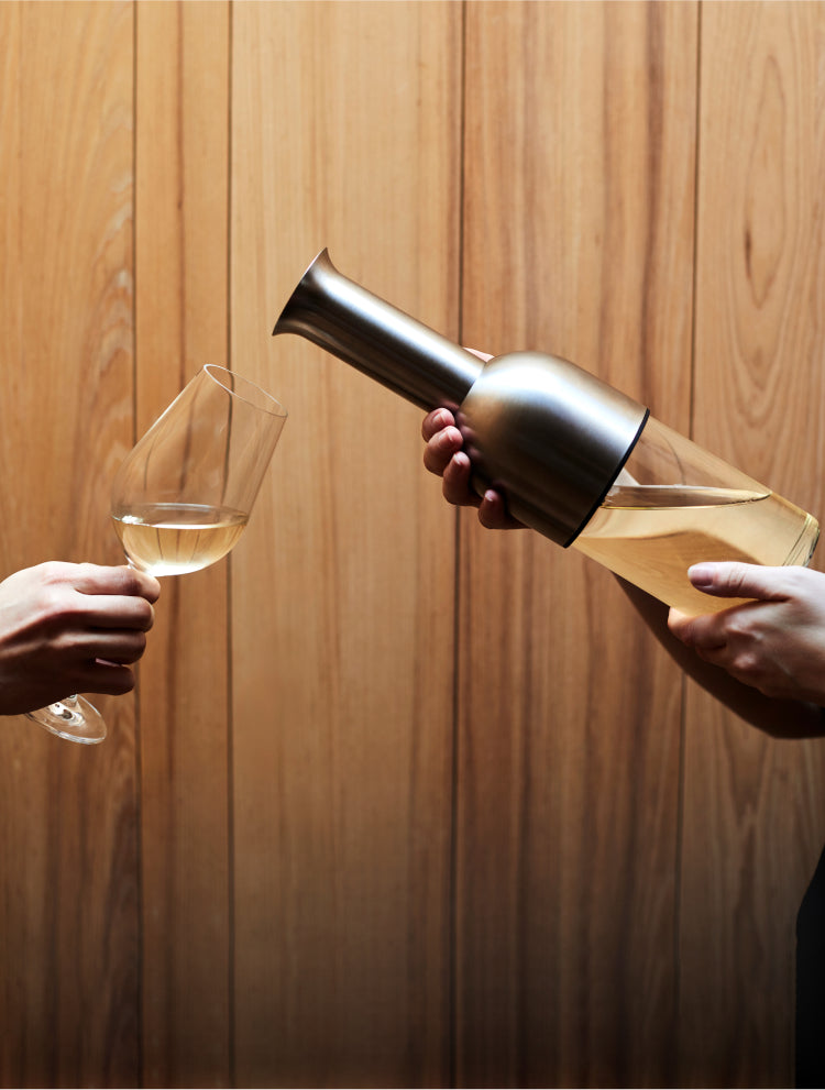 White wine is pour into an outstretched glass from the ETO wine decanter on a wooden backdrop