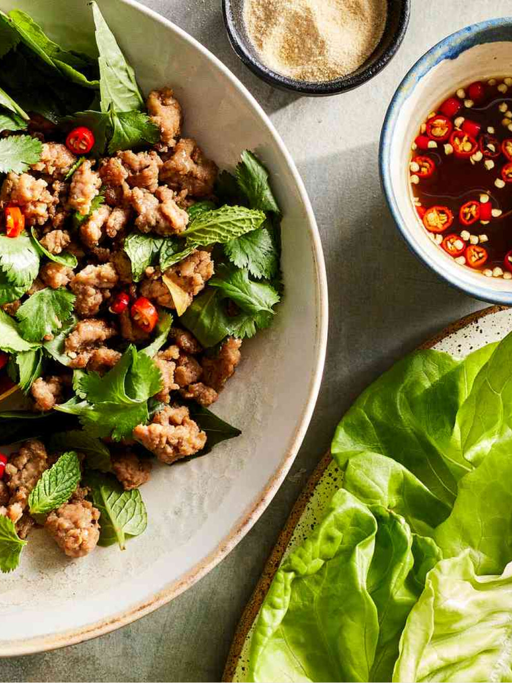 Plated dish with ground meat and greens, accompanied by a side of lettuce and sauces.