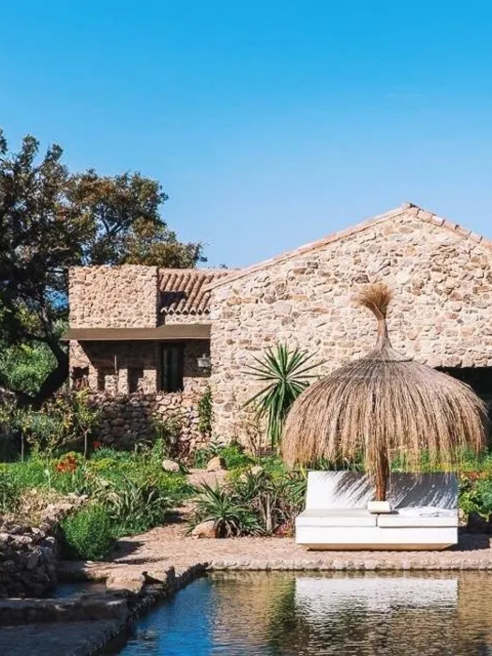 Stone building with a thatched umbrella by a pond and garden