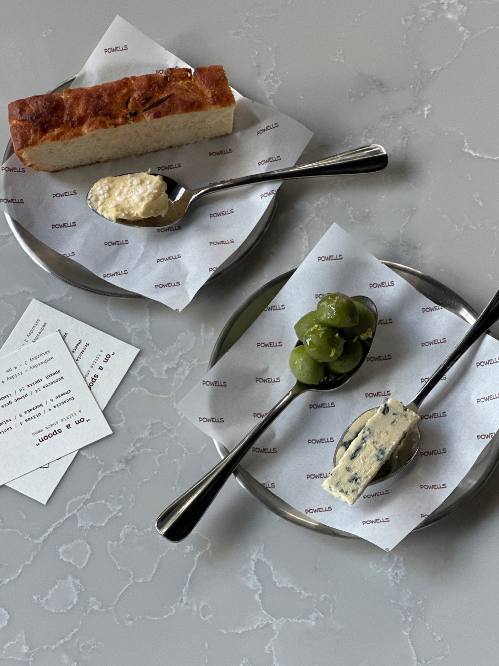 Two plates with bread, butter, blue cheese and olives on a gray surface