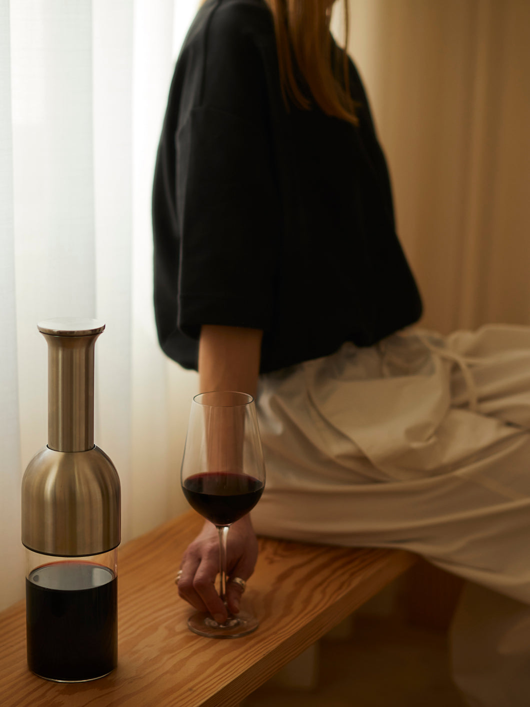 A stainless satin eto wine decanter on a bench beside a woman with a glass of wine