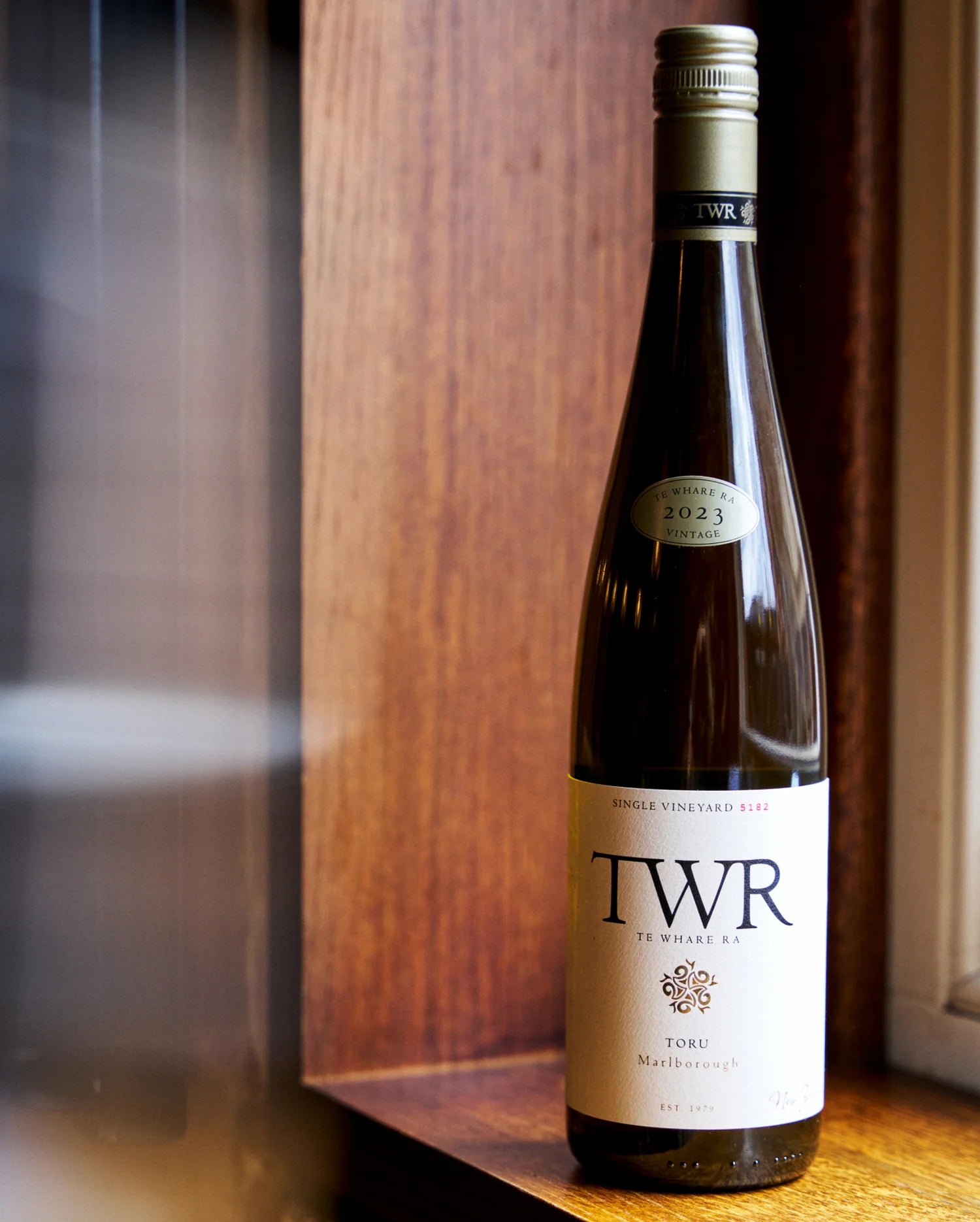A bottle of Te Whare Ra Toru on a wooden surface with bokeh 