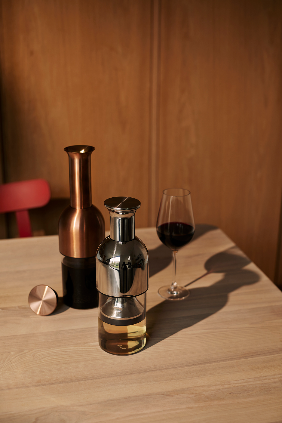 Two ETO wine decanters in Copper Satin and Stainless Mirror with red and white wine on a wooden table 
