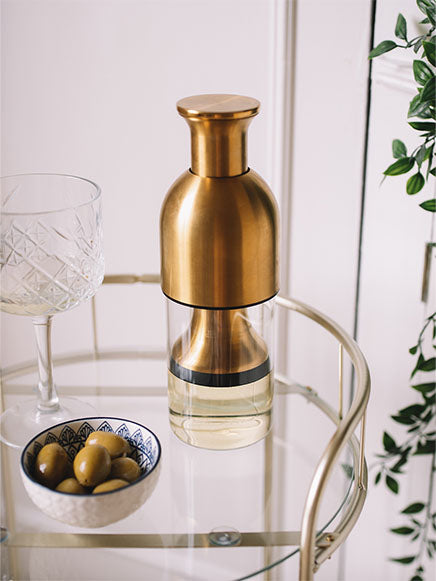 eto wine preserving decanter in brass satin finish on top of a glass bar cart with a small bowl of olives and a glass of white wine