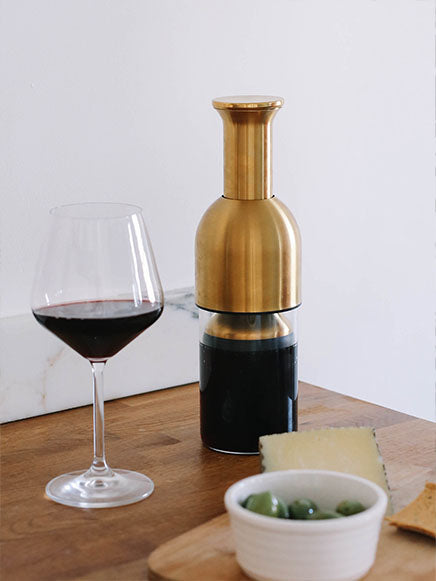 eto wine preserving decanter in brass satin finish on top of a wooden table with a glass of red wine
