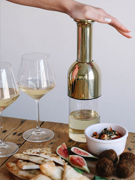 an eto wine decanter being pushed down its plunger filled with white wine next to a spread of Mediterranean food and two glasses of white wine