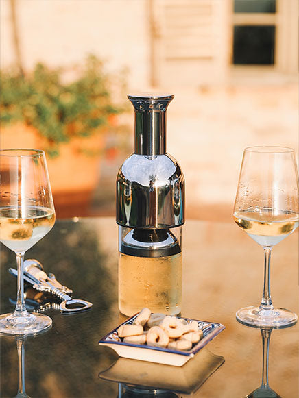 eto wine decanter in stainless steel in between two glasses of white wine on top of a glass table in the garden